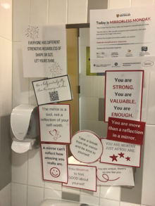 A washroom mirror partially covered with inspirational messages about body positivity.