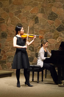 Ashley Yip plays the violin, wearing a black dress.