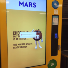 A yellow M&amp;Ms candy vending machine with an error message on its front screen.
