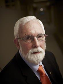 A profile shot of Professor Emeritus Mark Zanna. He has a white beard and is wearing a suit and red tie.