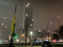 Campus flagpoles with a highrise shrouded in fog in the early morning.