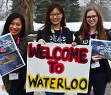 Three women hold a &quot;welcome to Waterloo&quot; sign at the March Break Open House.