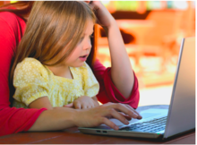 A child sits in their parent's lap while looking at a laptop.