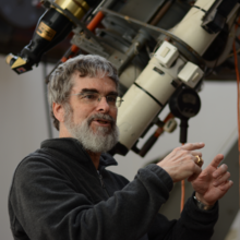 Brother Guy Consolmagno SJ stands next to a telescope.