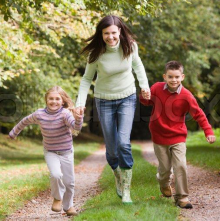 A mother and two children run along a wooded path.