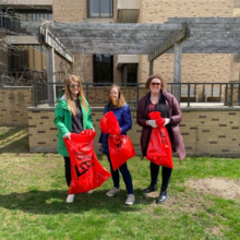 Three Earth Day campus clean-up volunteers holding red garbage bags.