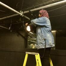 May Nemat Allah stands on a stepladder adjusting stage lights.