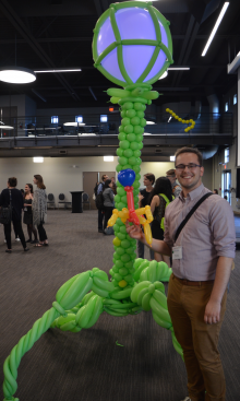 A man stands next to a large balloon construct that looks like a giant bacteriophage.