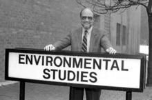 Professor James Bater (c1984) shows off the sign that marks the Faculty of Environment as a bus stop on the Ring Road.