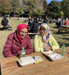Two women in headscarves sit at a picnic table.