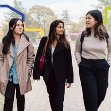 Three young women walk on a campus pathway.