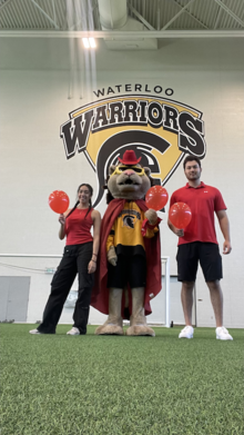 Two Athletics employees with King Warrior in red.