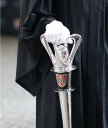 A gloved hand grips the University mace.