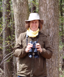 Bev Raimbault in birdwatching gear holding a pair of binoculars.