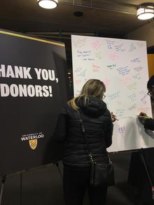 Students sign a poster-sized donor card to thank donors for their support.