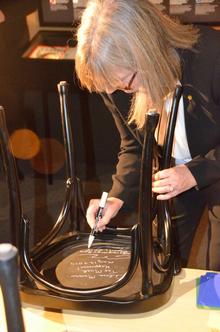 Donna Strickland autographs the underside of a chair at Bistro Nobel.