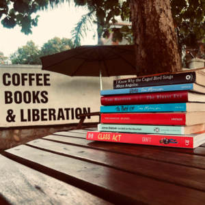 A stack of books next to a sign that says &quot;Coffee, Books, and Liberation.&quot;