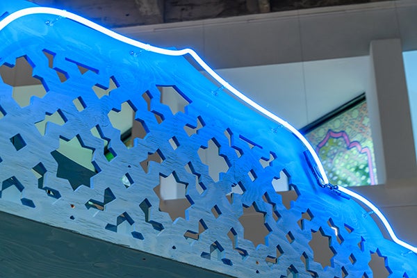A blue lattice archway with Islamic geometrics lit by a neon light.
