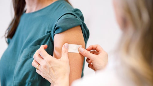 A person places a band-aid over an injection site on a person's arm.