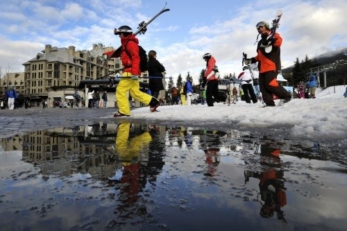 Skiiers carry their skis over a puddle in Whistler, BC.