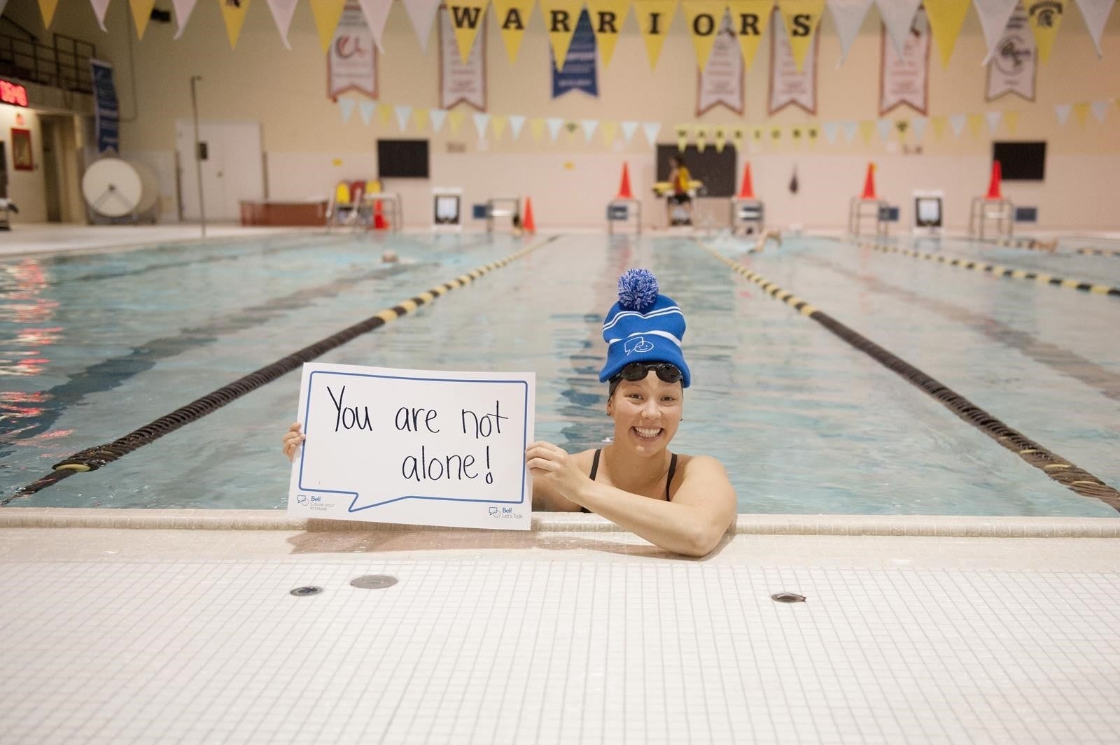 A swimmer in the Waterloo pool holds a sign saying "You are not alone."