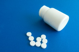 An unlabeled white pill bottle and a scattering of white pills against a blue background.