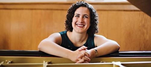 Pianist Mary Castello smiles while seated at a piano.