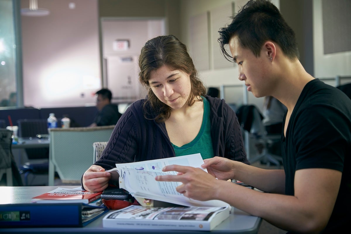 Male and female looking at a text book together, studying with math textbooks scattered around them.