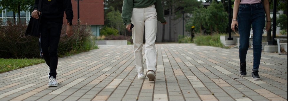 A picture of three students from the waist down walking on a campus pathway.