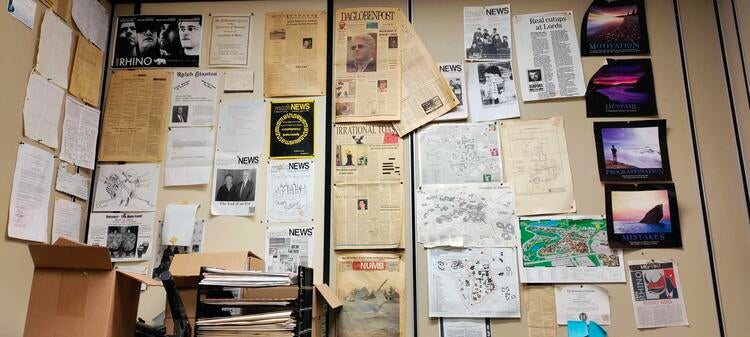 A wall in the mathNEWS office covered with previous issues, bits of posters and paper detritus, and demotivational posters.