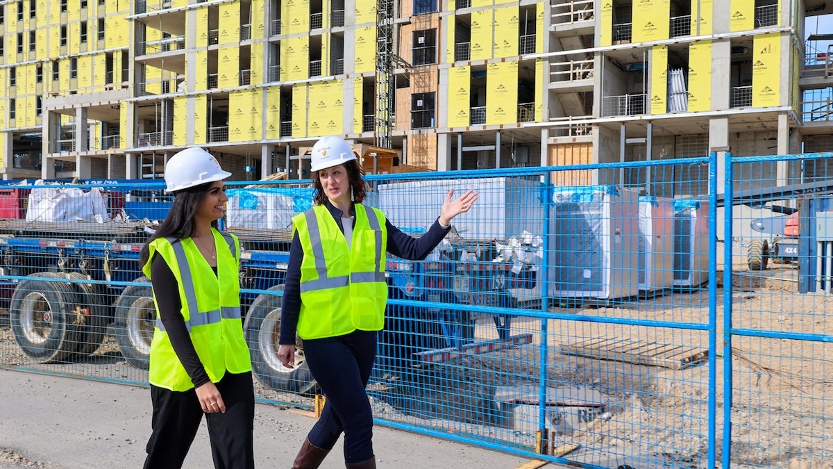 Dr. Leia Minaker and a young woman wear hard hats as they walk past a construction site.