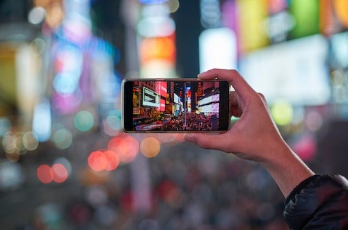 A person takes a smartphone photo of a busy urban setting.