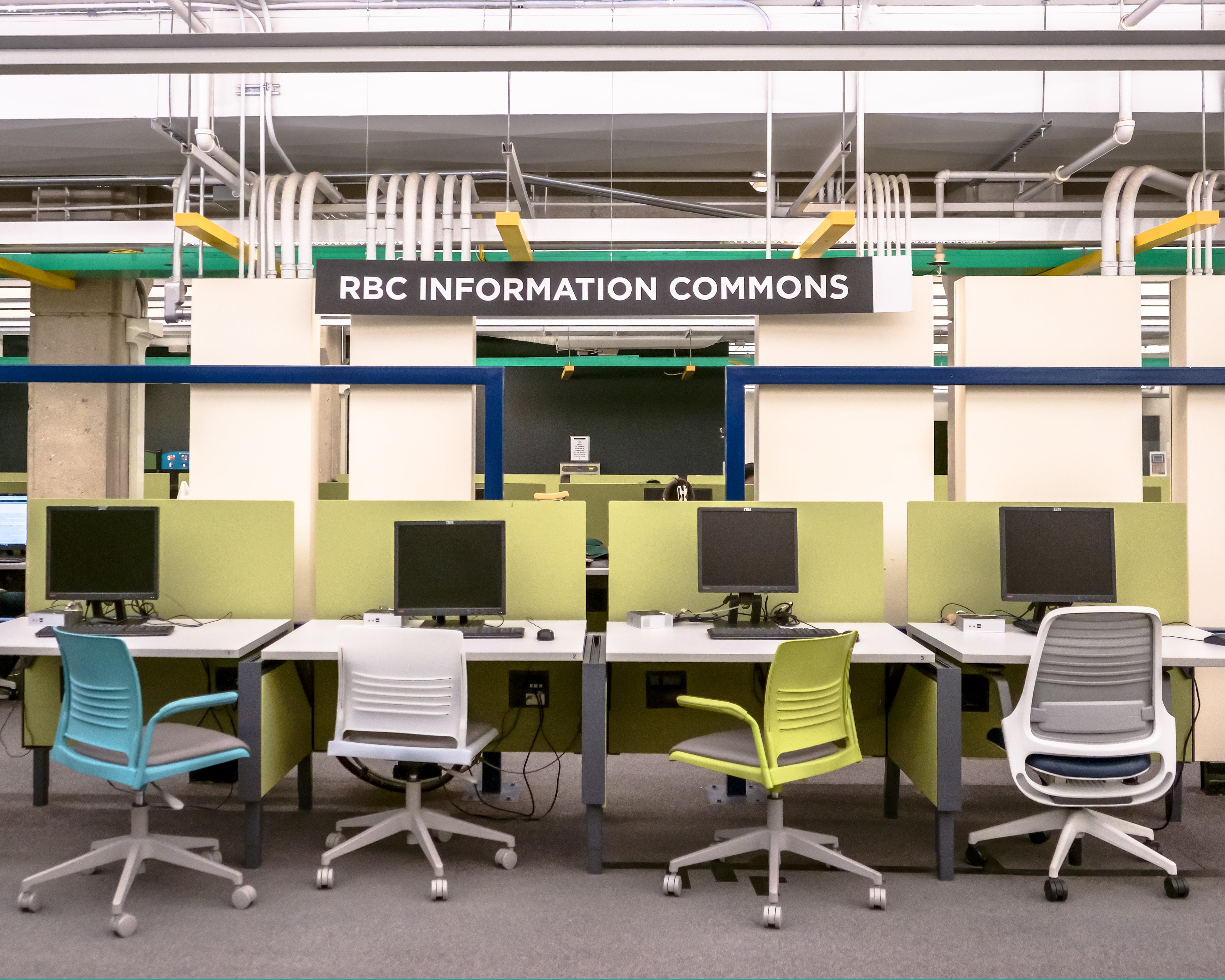 An interior view of a study area called "RBC Information Commons." Several computer desks are arranged in rows, each with a computer monitor.