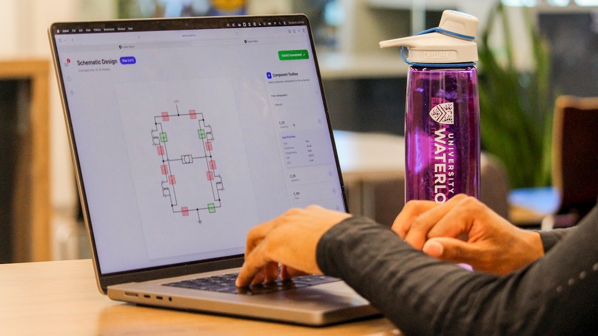 a person uses a laptop with a University of Waterloo water bottle in the background.