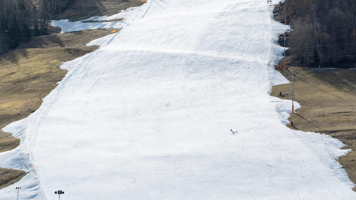 A skier goes down a downhill ski course that shows bare dry ground on either side.