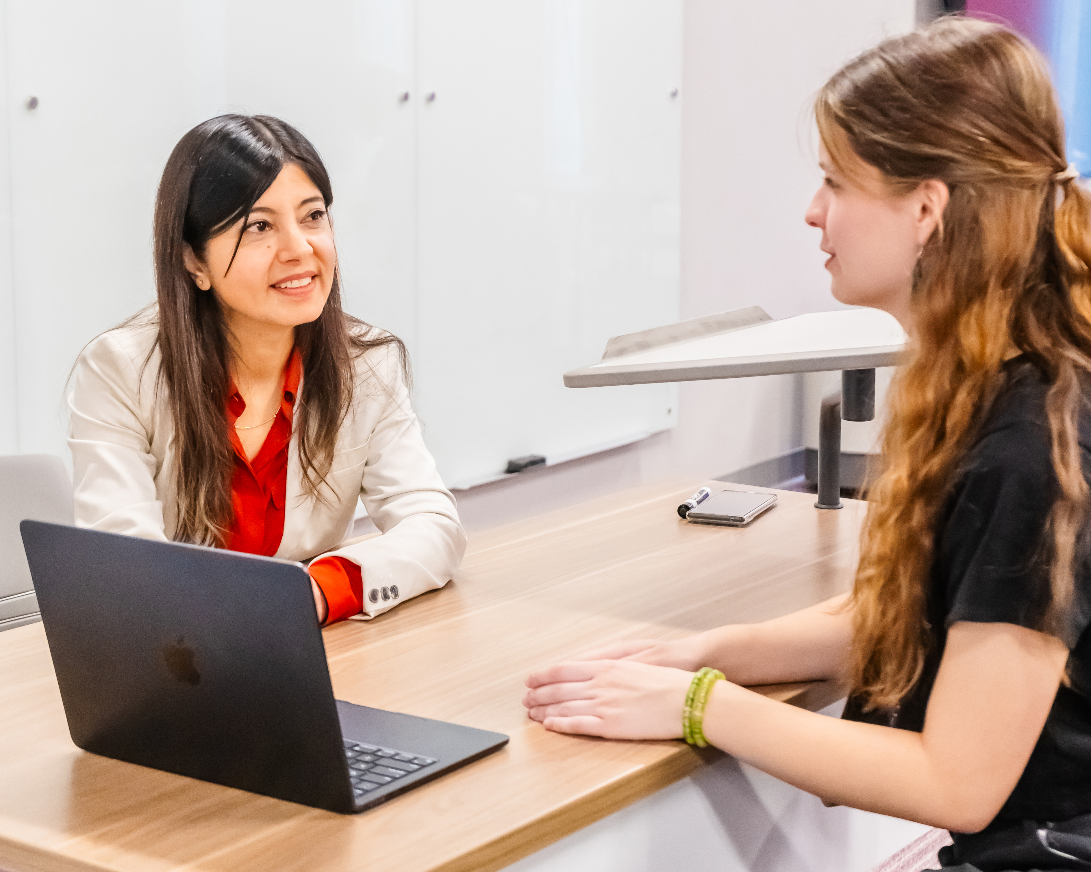 Two women in conversation with an open laptop between them.
