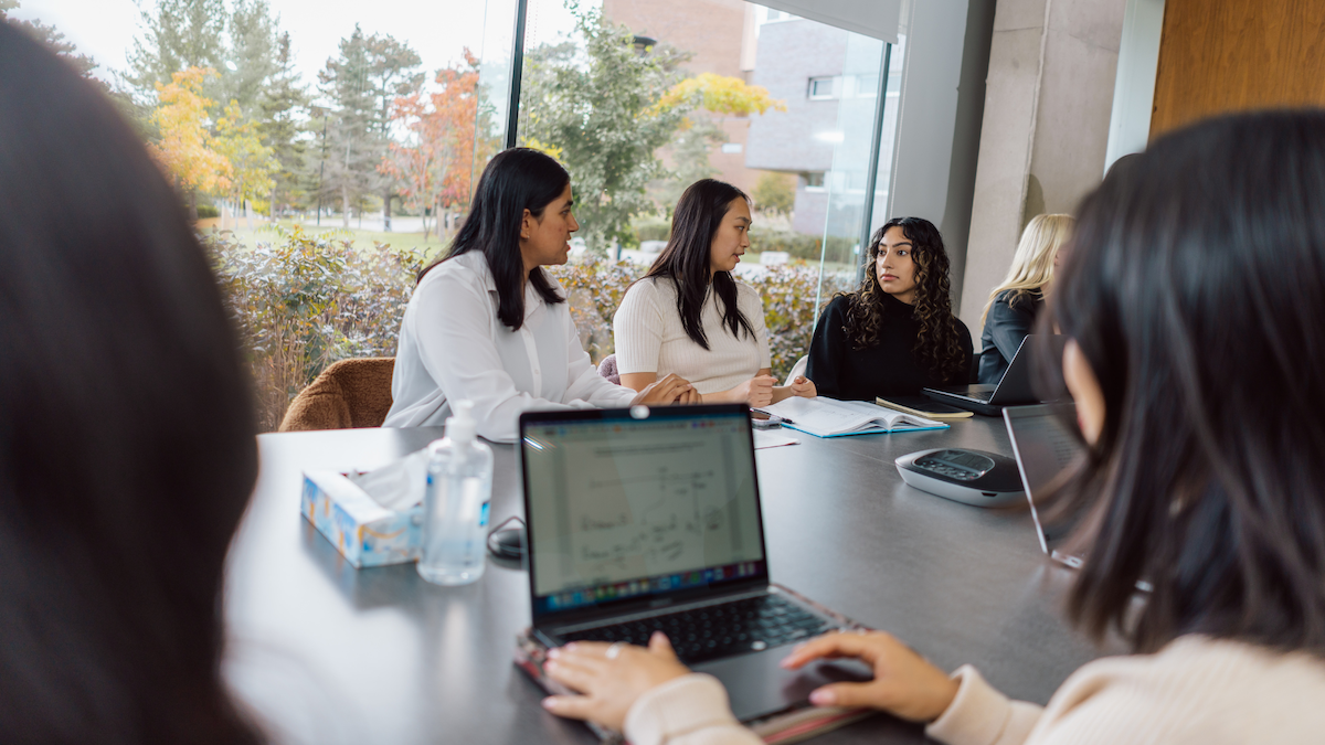 Students collaborating at a table with a computer in the foreground.