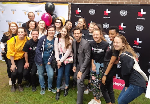 Students and staff pose for a group photo in front of a HeForShe banner.