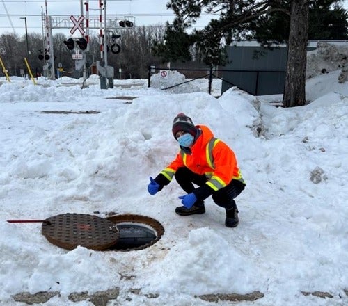 Biochemistry student Zach Miller crouches next to an open manhole on campus.