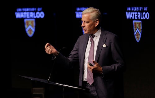 Dominic Barton speaks with the University of Waterloo logo behind him.