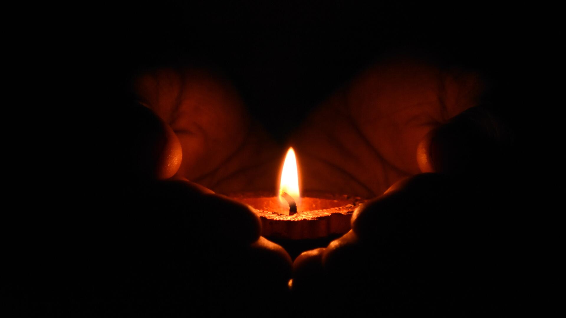 A lit candle cupped in a person's hands.