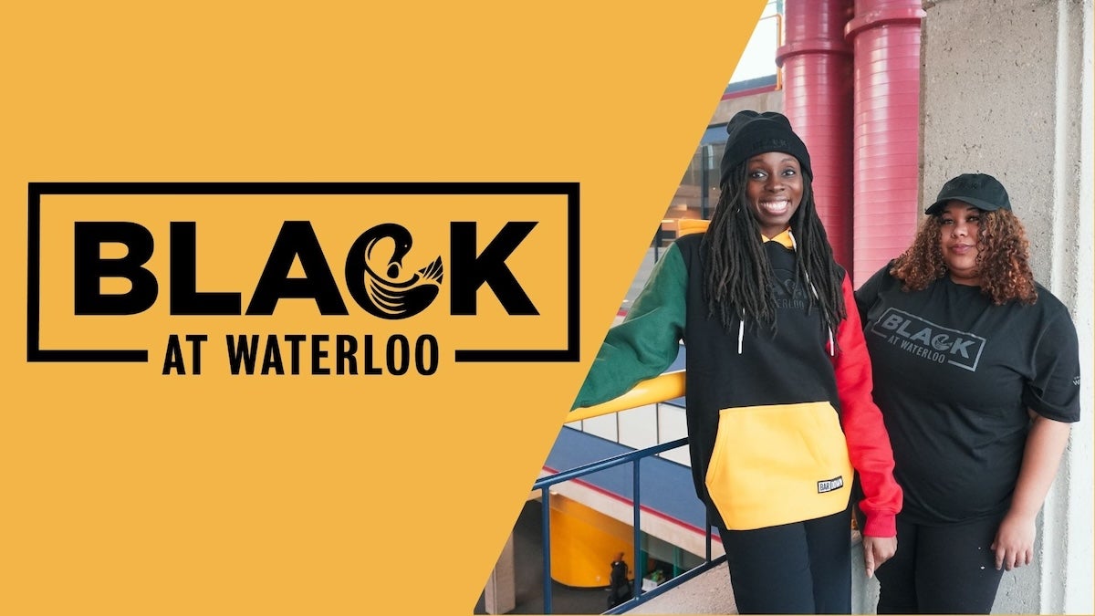 Two smiling women stand indoors beside a railing, wearing black “Black at Waterloo” apparel. 