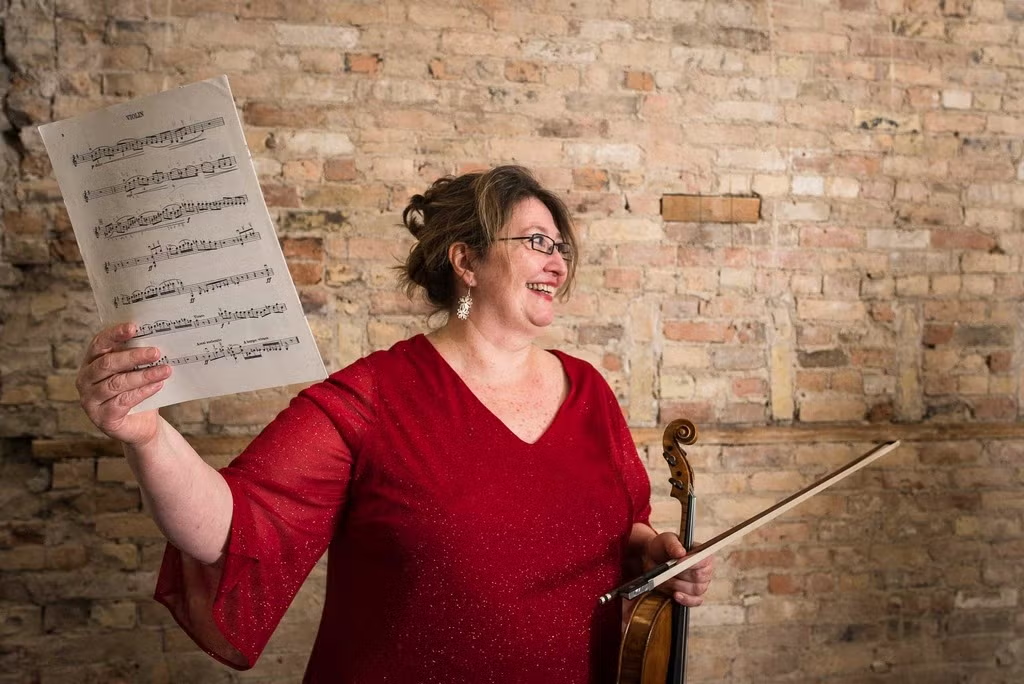 Annette Barbara Vogel holds sheet music in one hand and her violin and bow in the other.