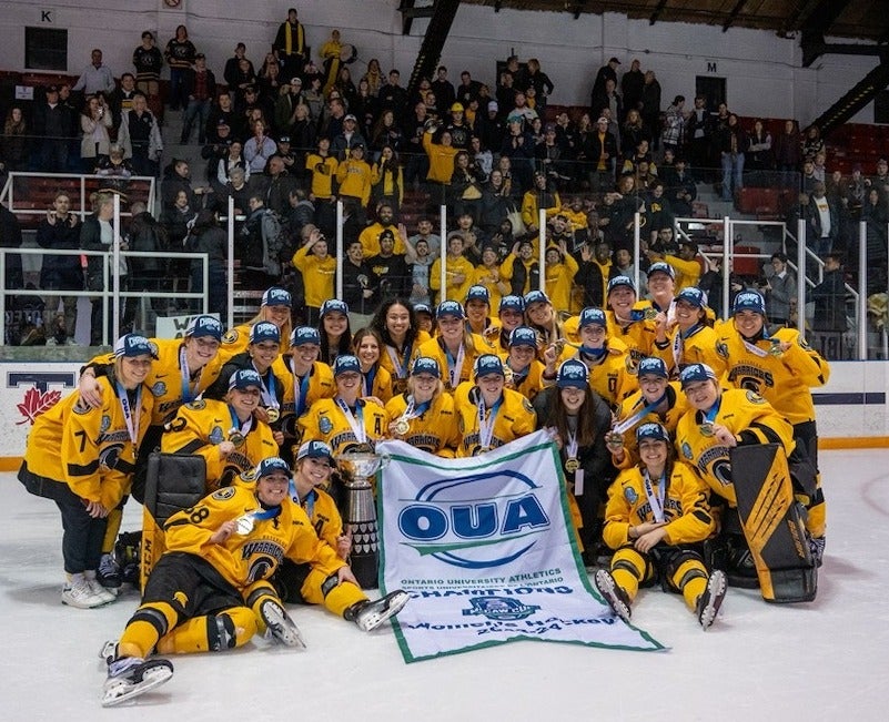 The Warriors women's hockey team pose for a group photo on the ice with their medals.