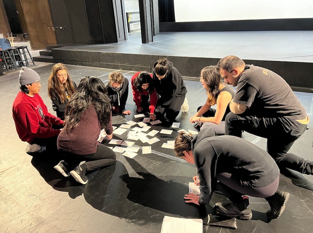 Immolation stage crew kneel down to consult file cards spread out on the floor of the stage at the Theatre of the Arts.