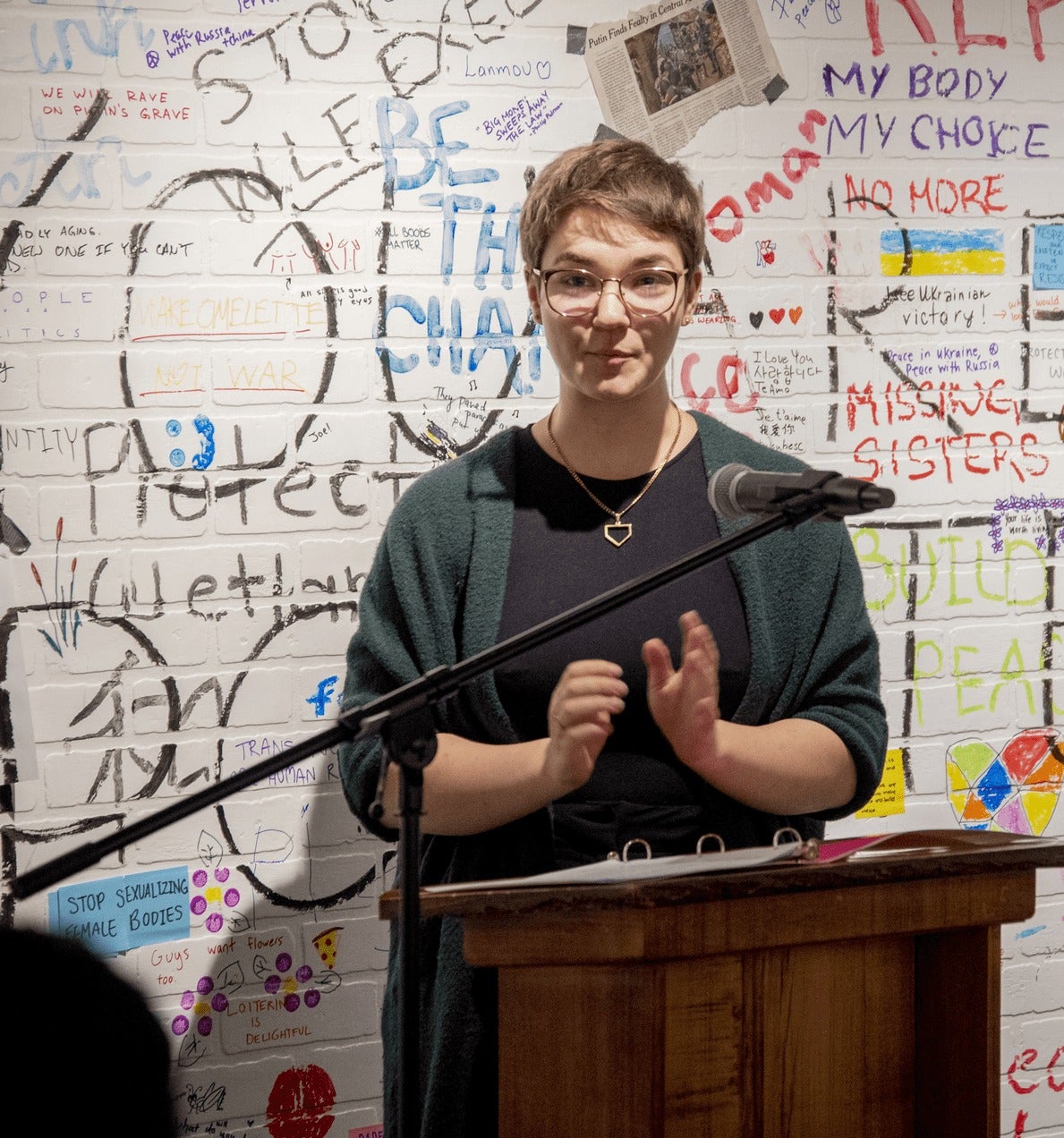 A person delivers a speech in front of a wall scrawled with political messages.