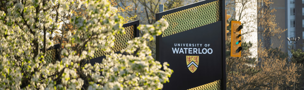 The University of Waterloo sign at the south entrance with blossoming trees in the foreground.