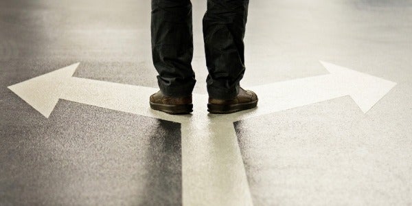 A person stands on top of two arrows pointing in opposite directions.