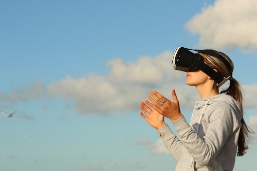 A woman stands outside while wearing a VR headset.