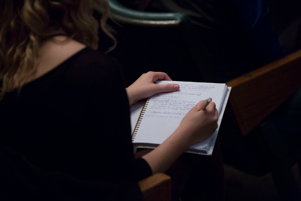 A woman takes notes at a lecture in a notebook.
